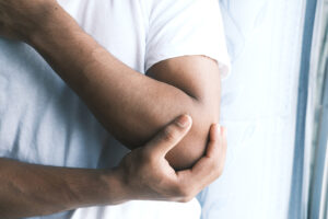 Man in white T-shirt clutching painful elbow