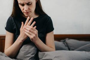 Woman sitting on her bed rubbing her painful arthritic hand