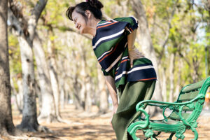 Woman touching her painful hip as she gets up from a park bench