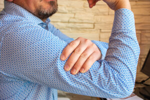 Man in blue shirt rubbing his painful biceps muscle